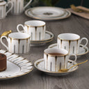 Ceramic tea set with cups, saucers, and a cake on a wooden table.