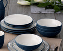 Blue and white ceramic dinnerware set on a wooden table with placemats and cutlery.